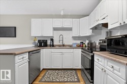 Kitchen featuring electric stove, a peninsula, white cabinetry, dishwasher, and a textured ceiling - 