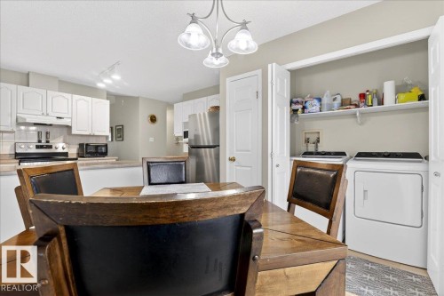 Kitchen with white cabinetry, light countertops, stainless steel appliances, washing machine and clothes dryer, and a chandelier - 13217 155 Avenue Nw, Edmonton, AB - Indoor Photo Showing Laundry Room