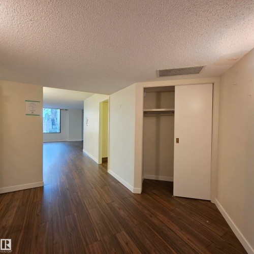 Unfurnished bedroom featuring a textured ceiling, dark wood-style flooring, and a closet - 2C 10050 118 Street, Edmonton, AB - Indoor Photo Showing Other Room