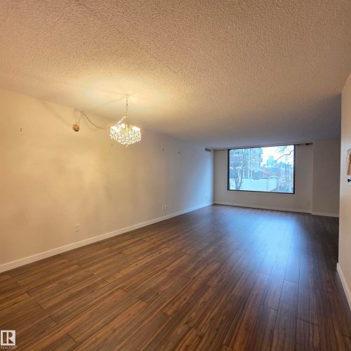 Empty room featuring a chandelier, a textured ceiling, and dark wood-type flooring - 2C 10050 118 Street, Edmonton, AB - Indoor Photo Showing Other Room