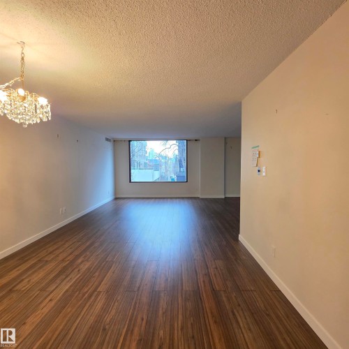 Empty room featuring a chandelier, a textured ceiling, and dark wood-type flooring - 2C 10050 118 Street, Edmonton, AB - Indoor Photo Showing Other Room