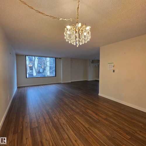 Spare room with a chandelier, a textured ceiling, and dark wood-style flooring - 2C 10050 118 Street, Edmonton, AB - Indoor Photo Showing Other Room