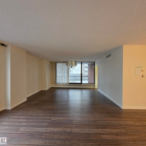 Empty room featuring expansive windows, a textured ceiling, dark wood finished floors, hanging lights, and baseboard heating - 2C 10050 118 Street, Edmonton, AB - Indoor Photo Showing Other Room
