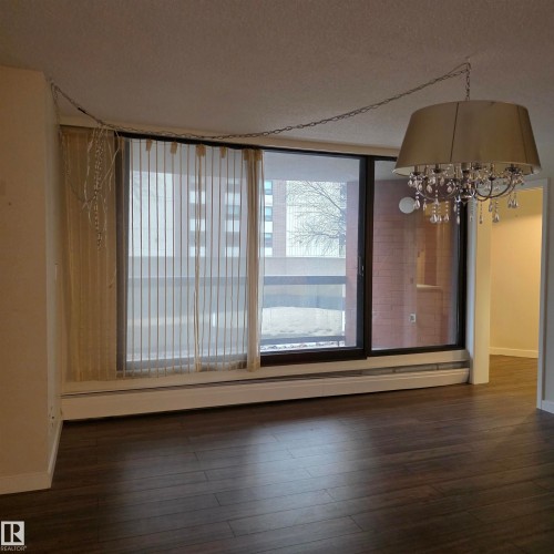 Unfurnished dining area featuring a textured ceiling, dark wood-style flooring, suspended lighting, and a baseboard heating unit - 2C 10050 118 Street, Edmonton, AB - Indoor Photo Showing Other Room