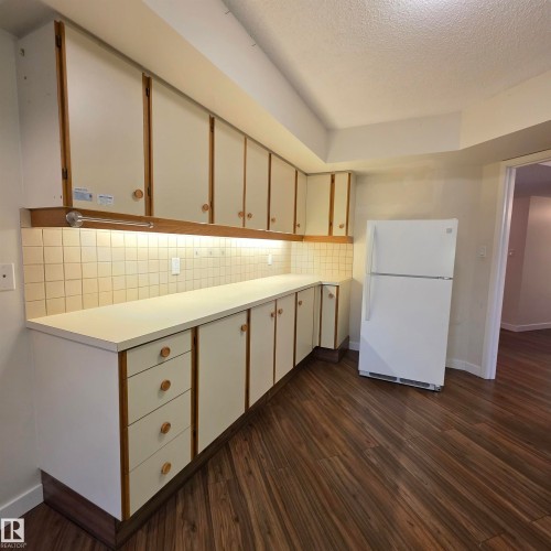 Dual tone kitchen featuring light countertops, freestanding refrigerator, tasteful backsplash, dark wood-type flooring, and dual tone cabinets - 2C 10050 118 Street, Edmonton, AB - Indoor Photo Showing Kitchen