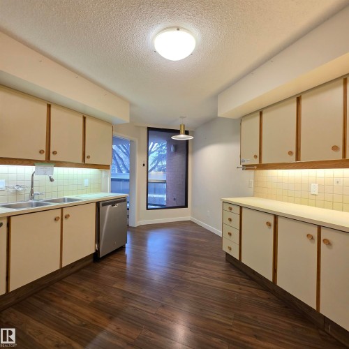 Two tone kitchen with backsplash, light countertops, dark wood-type flooring, two tone cabinetry, and stainless steel dishwasher - 2C 10050 118 Street, Edmonton, AB - Indoor Photo Showing Kitchen With Double Sink