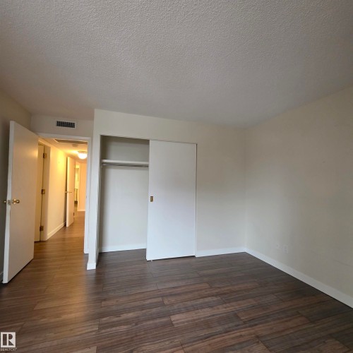 Unfurnished bedroom with dark wood-style floors, a textured ceiling, and a closet - 2C 10050 118 Street, Edmonton, AB - Indoor Photo Showing Other Room