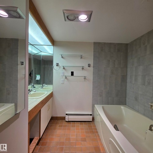 Full bathroom with a garden tub, double vanity, light tile patterned floors, and baseboard heating - 2C 10050 118 Street, Edmonton, AB - Indoor Photo Showing Bathroom