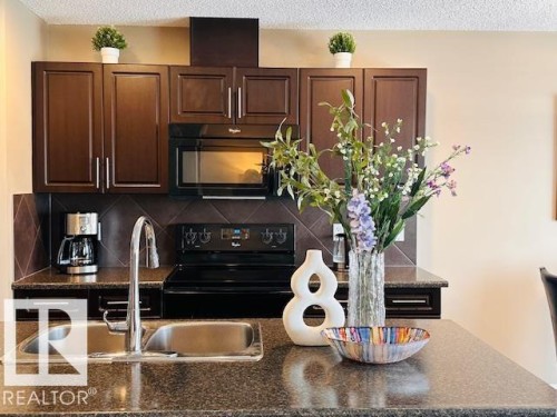 Kitchen featuring black appliances, a textured ceiling, dark wood finish cabinets, backsplash, and dark stone countertops - 12219 167A Avenue, Edmonton, AB - Indoor Photo Showing Kitchen With Double Sink