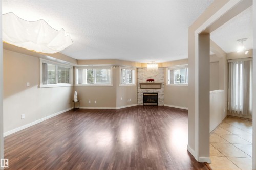 Unfurnished living room featuring a textured ceiling, dark wood-style flooring, and a fireplace - 113 10311 111 Street, Edmonton, AB - Indoor