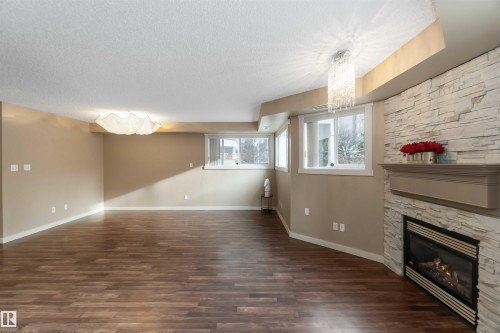 Unfurnished living room featuring a fireplace, hanging lights, dark wood-type flooring, and a textured ceiling - 113 10311 111 Street, Edmonton, AB - Indoor With Fireplace
