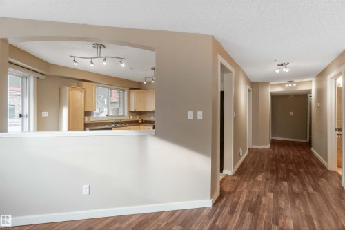 Kitchen with light wood finish cabinets, dark wood-style flooring, a textured ceiling, and light countertops - 113 10311 111 Street, Edmonton, AB - Indoor Photo Showing Other Room