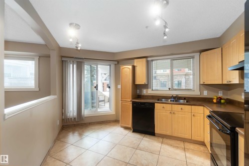 Kitchen with black appliances, dark countertops, light wood finish cabinetry, and light tile patterned flooring - 113 10311 111 Street, Edmonton, AB - Indoor Photo Showing Kitchen With Double Sink