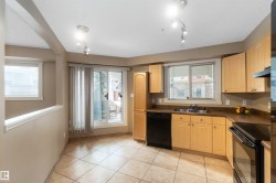 Kitchen with black appliances, dark countertops, light wood finish cabinetry, and light tile patterned flooring - 