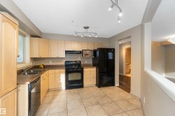 Kitchen featuring black appliances, a textured ceiling, light wood finish cabinetry, dark countertops, and light tile patterned floors - 