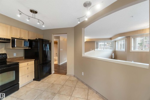 Kitchen featuring light wood finish cabinets, black appliances, light tile patterned floors, and rail lighting - 113 10311 111 Street, Edmonton, AB - Indoor Photo Showing Kitchen