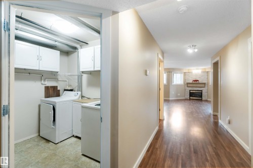 Laundry area with cabinet space, washer / clothes dryer, and a stone fireplace - 113 10311 111 Street, Edmonton, AB - Indoor Photo Showing Laundry Room