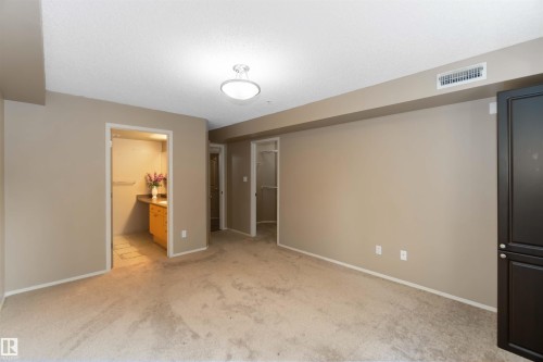 Unfurnished bedroom with a walk in closet, light colored carpet, and connected bathroom - 113 10311 111 Street, Edmonton, AB - Indoor Photo Showing Other Room