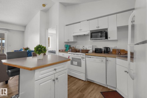 Kitchen featuring white appliances, white cabinets, light wood-style floors, and a high textured ceiling - 502 7511 171 Street Nw, Edmonton, AB - Indoor Photo Showing Kitchen