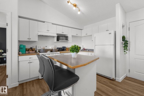 Kitchen featuring freestanding refrigerator, white cabinets, dark wood-style floors, a kitchen bar, and stainless steel microwave - 502 7511 171 Street Nw, Edmonton, AB - Indoor