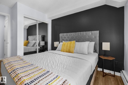 Bedroom with a textured ceiling, baseboard heating, a closet, and wood finished floors - 502 7511 171 Street Nw, Edmonton, AB - Indoor Photo Showing Bedroom