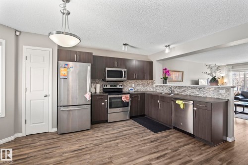 Kitchen with dark countertops, dark wood finish cabinets, stainless steel appliances, decorative light fixtures, and a textured ceiling - 3221 Cherry Cres Sw, Edmonton, AB - Indoor Photo Showing Kitchen