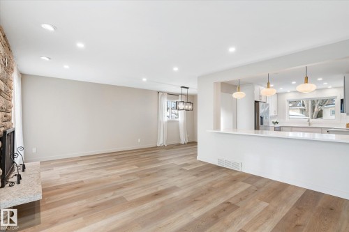 Unfurnished living room with light wood-style flooring, recessed lighting, and a stone fireplace - 4120 108 Street, Edmonton, AB - Indoor Photo Showing Kitchen