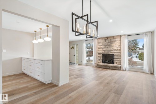 Unfurnished living room with light wood-style flooring, a fireplace, and hanging lights - 4120 108 Street, Edmonton, AB - Indoor Photo Showing Living Room With Fireplace