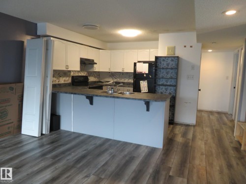 Kitchen featuring dark countertops, white cabinetry, dark wood-style floors, black appliances, and a kitchen bar - 2945 26 Street, Edmonton, AB - Indoor Photo Showing Kitchen