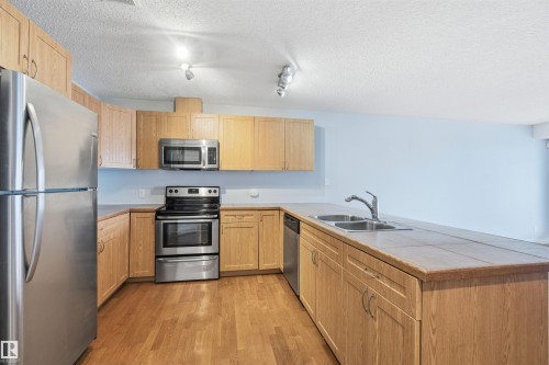 Kitchen featuring appliances with stainless steel finishes, a peninsula, light wood finished floors, light brown cabinetry, and a textured ceiling - 2953 26 Street, Edmonton, AB - Indoor Photo Showing Kitchen With Stainless Steel Kitchen With Double Sink
