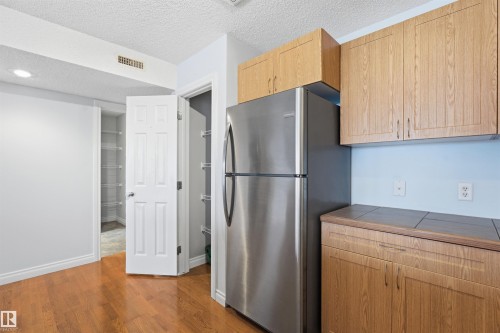 Kitchen with tile countertops, freestanding refrigerator, a textured ceiling, light brown cabinets, and dark wood-type flooring - 2953 26 Street, Edmonton, AB - Indoor