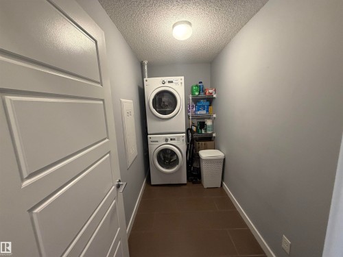 Laundry area with a textured ceiling and stacked washing machine and dryer - 417 1004 Rosenthal Boulevard, Edmonton, AB - Indoor Photo Showing Laundry Room