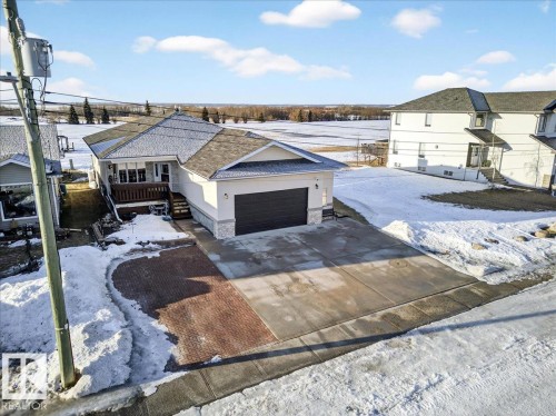 View of front of house featuring stone siding, driveway, an attached garage, a wooden deck, and stucco siding - 5019 48 Avenue, Chipman, AB - Outdoor