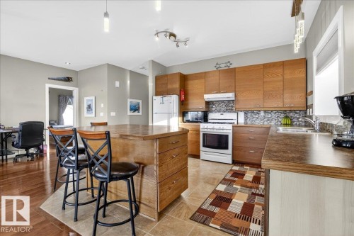 Kitchen with wood finish cabinets, white appliances, a kitchen breakfast bar, and hanging light fixtures - 5019 48 Avenue, Chipman, AB - Indoor Photo Showing Kitchen With Double Sink