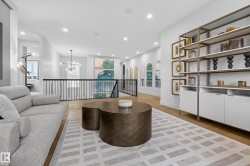 Sitting room with light wood-style floors, suspended lighting, and an upstairs landing - 