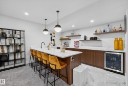 Indoor bar featuring open shelves, wine cooler, decorative light fixtures, modern cabinets, and light stone counters - 