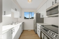 Kitchen with stainless steel appliances, white cabinets, and light wood-style flooring - 