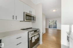 Kitchen with stainless steel appliances, white cabinetry, light stone counters, light wood-style flooring, and a textured ceiling - 