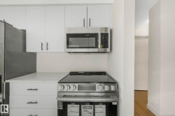 Kitchen featuring stainless steel appliances, white cabinets, wood finished floors, and light stone countertops - 
