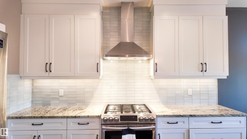 Kitchen featuring gas stove, light stone counters, white cabinetry, and tasteful backsplash - 10 Moberg Close, Leduc, AB - Indoor Photo Showing Kitchen With Upgraded Kitchen