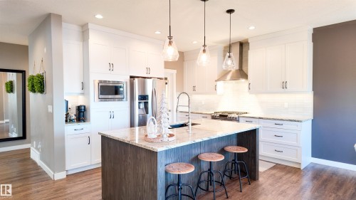 Two tone kitchen with a breakfast bar, a center island with sink, stainless steel appliances, light stone counters, and decorative light fixtures - 10 Moberg Close, Leduc, AB - Indoor Photo Showing Kitchen With Upgraded Kitchen