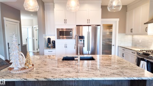 Kitchen with light stone countertops, stainless steel appliances, decorative backsplash, white cabinetry, and hanging light fixtures - 10 Moberg Close, Leduc, AB - Indoor Photo Showing Kitchen With Upgraded Kitchen