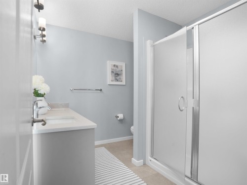 Full bath featuring a stall shower, double vanity, a textured ceiling, and light tile patterned floors - 207 41 Avenue, Edmonton, AB - Indoor Photo Showing Bathroom