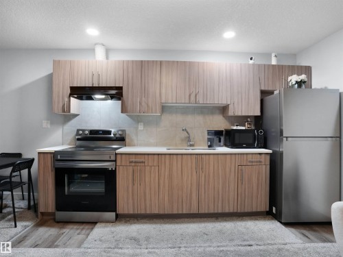 Kitchen featuring stainless steel appliances, decorative backsplash, a textured ceiling, light wood-style flooring, and modern cabinets - 207 41 Avenue, Edmonton, AB - Indoor Photo Showing Kitchen