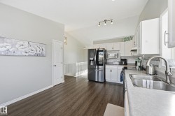 Kitchen with lofted ceiling, white cabinetry, stainless steel appliances, dark wood-style floors, and decorative backsplash - 