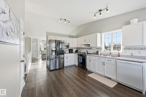 Kitchen with stainless steel appliances, white cabinetry, dark wood-type flooring, backsplash, and lofted ceiling - 2952 39 Avenue, Edmonton, AB - Indoor Photo Showing Kitchen