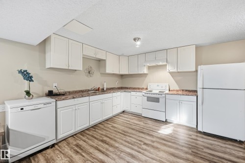 Kitchen with white appliances, white cabinetry, light wood-type flooring, and a textured ceiling - 2952 39 Avenue, Edmonton, AB - Indoor Photo Showing Kitchen