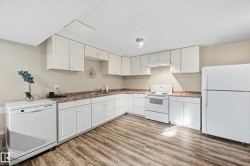 Kitchen with white appliances, white cabinetry, light wood-type flooring, and a textured ceiling - 