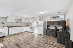Kitchen with white appliances, white cabinetry, light wood-style floors, and a textured ceiling - 