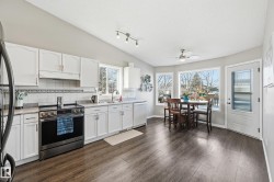 Kitchen with stainless steel appliances, white cabinetry, ceiling fan, dark wood finished floors, and light countertops - 